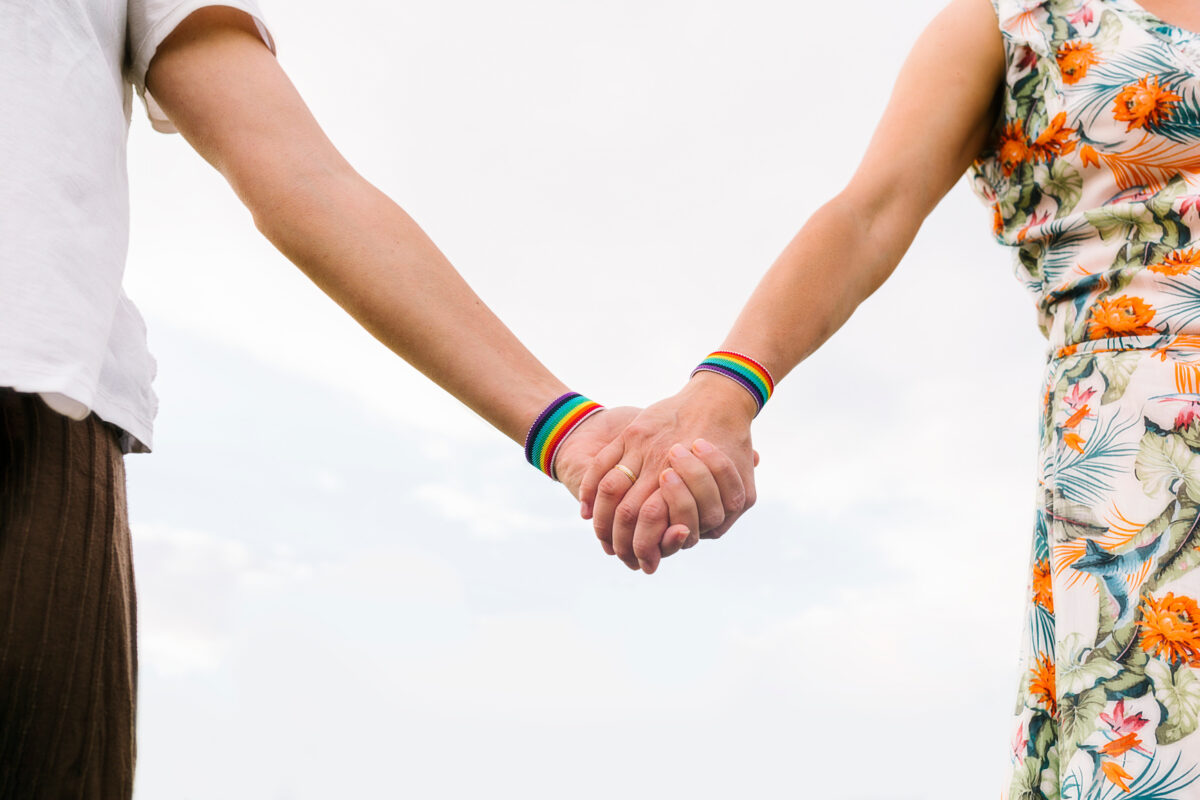 Lesbian women holding hands with lgbt bracelets in a summer day