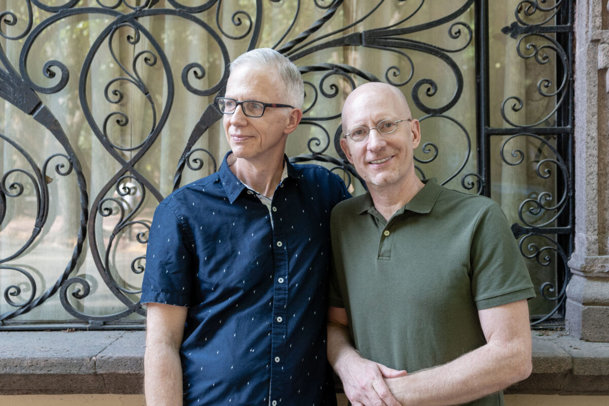 Gay couple of silver-age standing next to a colonial metal-work window