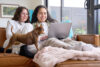 Young lesbian couple cuddle up on lounge watching movie on laptop